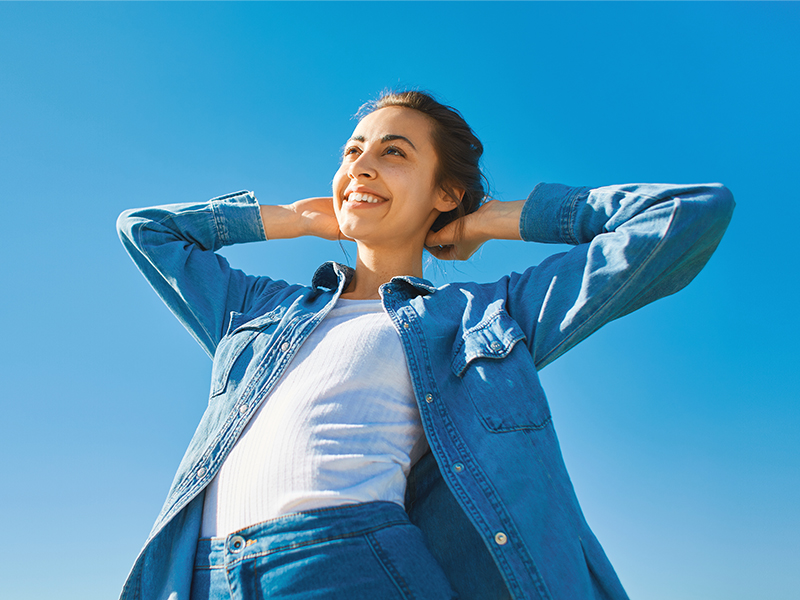 bottom view of a young smiling attractive woman in jeans clothes at sunny day on the blue sky background.